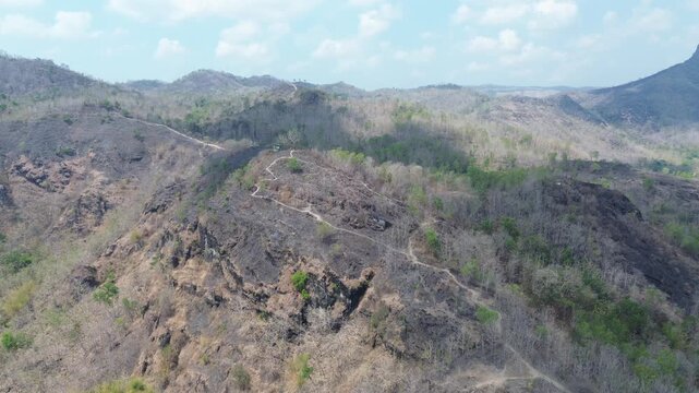 Aerial drone view of a winding trail on a dry rocky mountain ridge surrounded by hills under a bright sky. Landscape footage template for nature documentary and travel video.