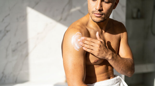 Young man applying moisturizing body lotion to shoulder after shower routine