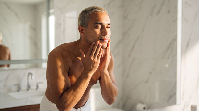 Content young man massaging moisturizer into skin with both hands closely