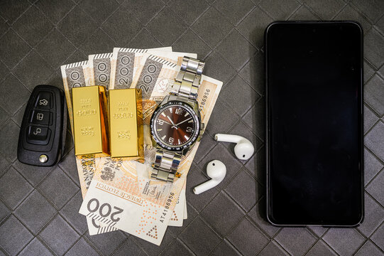 Men Watch Two Fine Gold Bullion Bars Car Key and Earbuds Resting over Polish Zloty Cash Stack