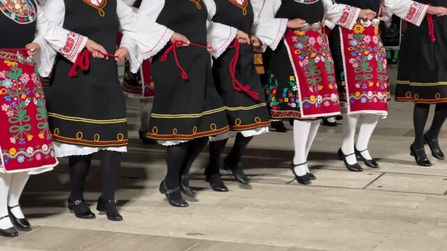 Cropped view of dancers performing traditional balkan folk dance on street in colorful embroidered national costumes and ethnic aprons during cultural festival.