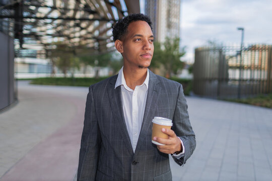 Young mixed race businessman walks in urban area holding a coffee cup