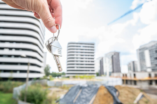 Open Palm Holding House Keys with Metal Keychain and Modern Building Construction Background