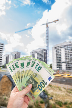 Male Hand Holding Stack of 100 Euro Banknotes Against Construction Site Building Exterior