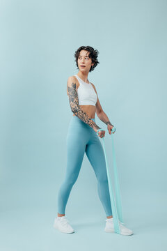 Full length of a young slim woman practicing with a resistance band over blue backdrop