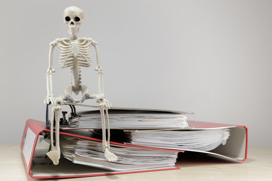 Skeleton Figure Sitting on Overflowing Office Binders