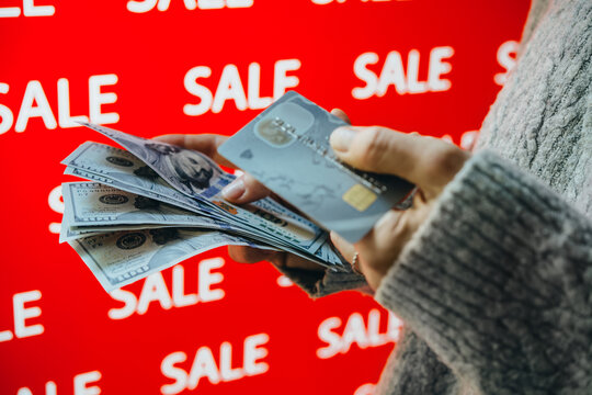Person holding US dollar banknotes and a bank card during sale shopping.