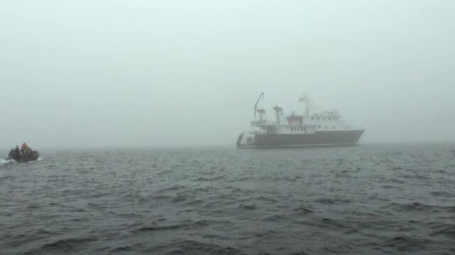 Arctic Expedition Ship Sailing Through Mist Across the Arctic Ocean. Cold open water and a distant polar horizon define the remote northern seascape beneath a pale sky.