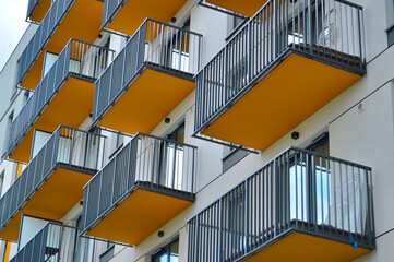 Modern apartment building facade featuring vibrant orange balconies with geometric metal railings arranged in a striking repetitive urban pattern © TannySolt