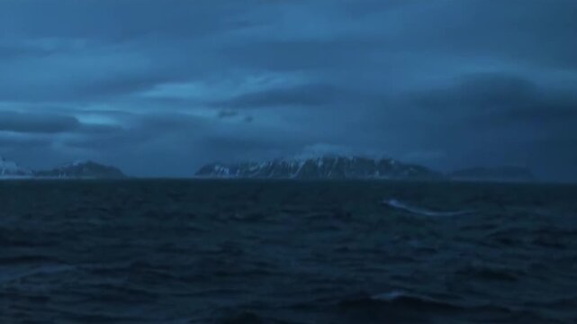 Arctic Ocean Ship Navigating Cold Arctic Ocean on a Northern Voyage. Snow-covered mountains remain visible beyond the cold open water and the distant polar horizon.