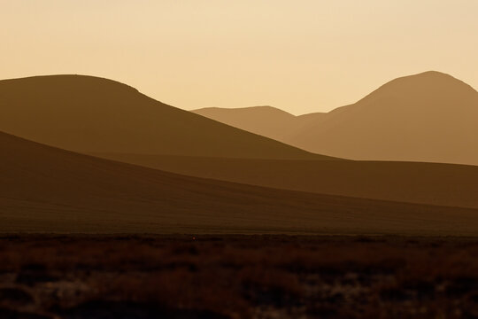 Volcanic hills at sunset in Fuerteventura, Canary Islands, Spain, layered mountain silhouette, golden haze, minimalist desert landscape near a popular wing foiling and kitesurfing coast