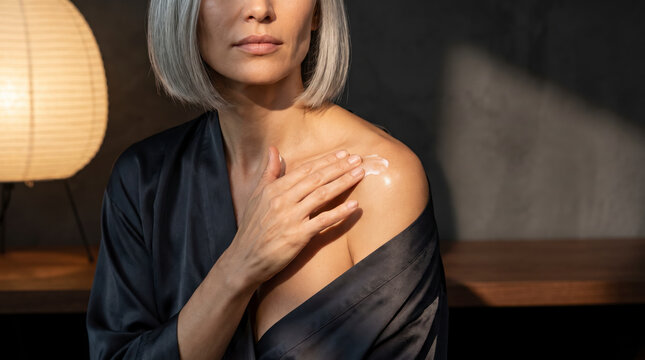 Mature woman applying moisturizer cream to her bare shoulder skin closeup