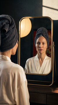 Mature woman with towel wrapped hair looking at her own mirror reflection