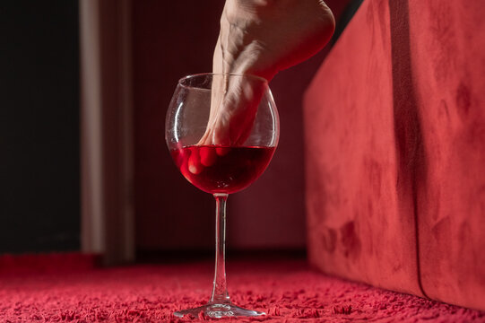 Foot fetish. A woman dips her toes in a glass of red wine.