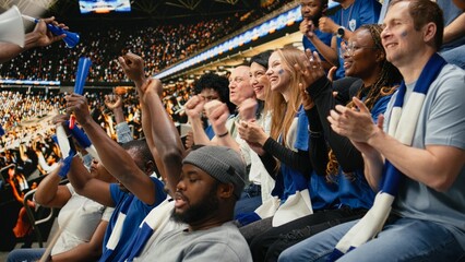 Obraz premium Blue football supporters cheer with raised scarves in a packed stadium during a live soccer match, showing emotional crowd reactions and fan chants.