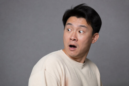 Surprised adult with wide eyes on gray background, shock and unexpected news concept