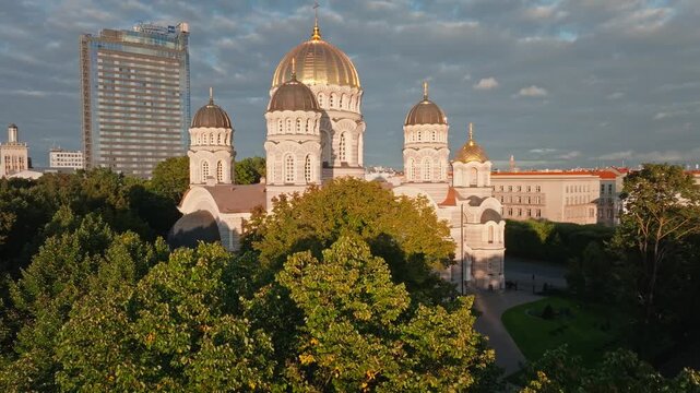 Nativity of Christ Cathedral revealed above park from drone, Riga. Aerial shot rising over park canopy in Riga, Latvia, to the golden domed orthodox church.