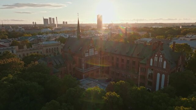 Art Academy of Latvia with sun flare at sunset from drone, Riga. Aerial shot approaching the red brick neo gothic academy in Riga, Latvia.