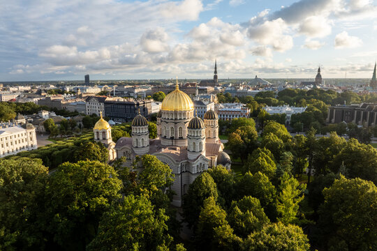 Nativity of Christ Cathedral in park under clouds from drone, Riga, Latvia. Aerial view of the golden domed church surrounded by park trees and lawns with historic buildings, old town spires.