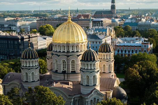 Nativity of Christ Cathedral domes close up from drone at golden hour, Riga. Drone close view of the gilded main dome, dark cupolas and crosses in warm light with St Peters spire.