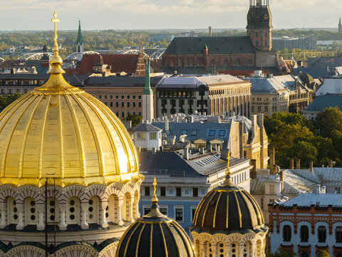 Golden cathedral dome with St Peters tower and Dome cathedral from drone, Riga, Latvia. Drone close telephoto view of the gilded main dome and cross in warm light with St Peters spire.