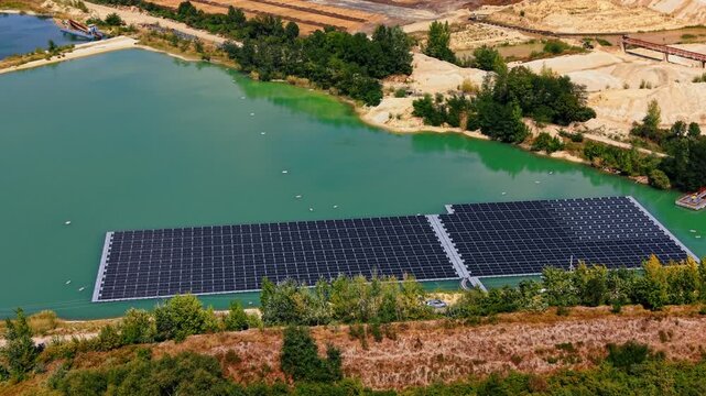 A large floating solar panel array deployed on a body of turquoise-green water. Industrial site, likely a sand or gravel quarry in the backdrop. Aerial view.