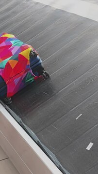 Brightly colored suitcase with a geometric pattern cover moving along a baggage reclaim belt at an airport terminal. Waiting for luggage