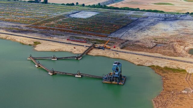 Industrial sand and gravel dredging operation located in a quarry lake. Floating dredger and conveyor belts on the turquoise water from drone.
