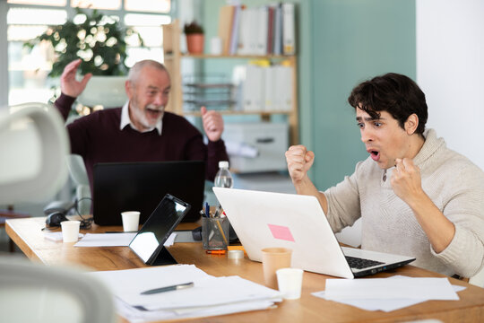 Men office employees is genuinely happy and elated. Colleague shares joy. Winning lottery, approving contract.