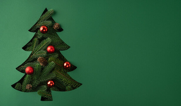Merry Christmas and Happy New Year creative vision with cutout Christmas tree and red ornaments on banner green background