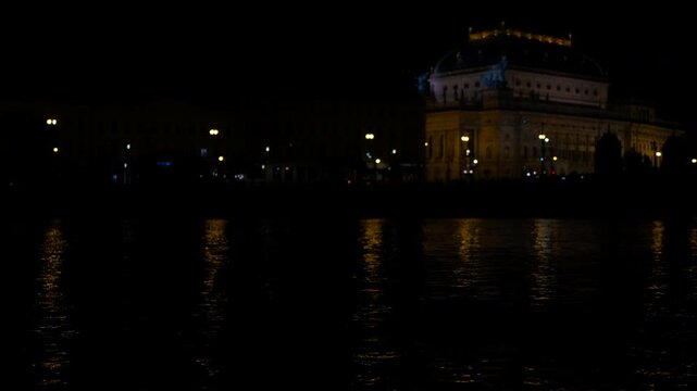 Boats passing by illuminated building at night. Water reflects vibrant city lights while boats glide past an illuminated building at night.