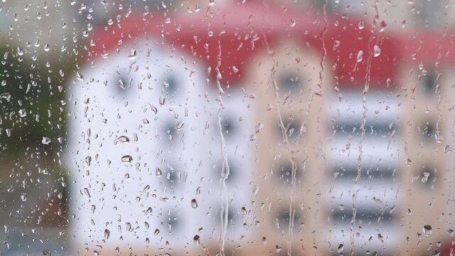 Modern building in rain through glass. A view of foggy window with raindrops against cityscape in autumn