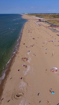 Vertical aerial drone video of Katwijk aan Zee sandy beach, North Sea coast, dunes, and beach pavilions stretching into distance in South Holland, Netherlands on sunny summer day