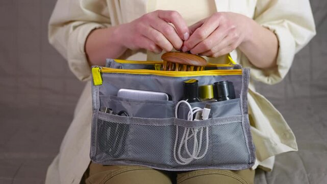 Woman organizing travel bag pouch with toiletries and gadgets. Organized woman putting personal care items, cosmetics, a massager, and electronic gadgets into a convenient travel pouch