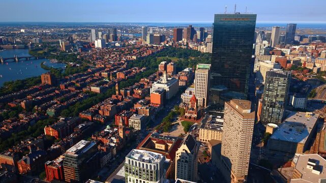 John Hancock Tower and Copley Square above the Boston cityscape. A glass skyscraper rises beside Trinity Church, with rows of brick houses and the river extending left.