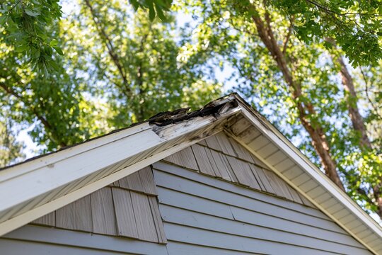 The roof of a weathered gable house with damaged shingles
