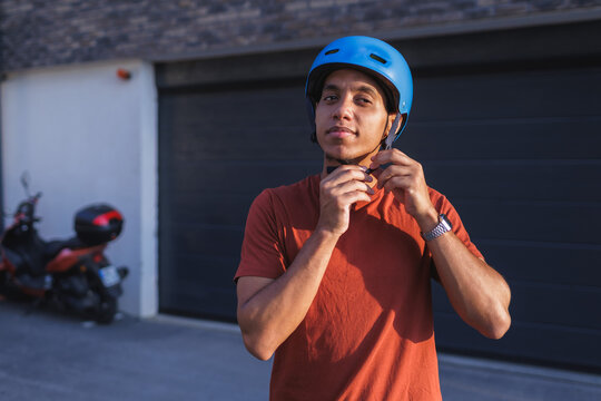 Man in a blue helmet adjusting straps stands outside in street