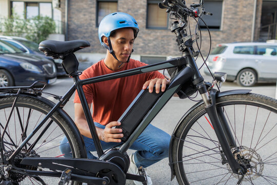 Electric bicycle battery maintenance, man changing power pack on e-bike outdoors