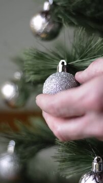 Close up of male hand placing silver ball on Christmas tree branch, static shot without visible faces