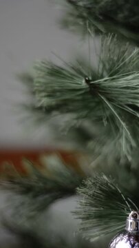 Close up of male hand decorating Christmas tree branches with silver baubles, static shot without visible faces