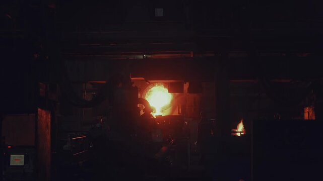Molten metal pouring from industrial ladle in foundry, high temperature metal casting process inside heavy manufacturing plant.
