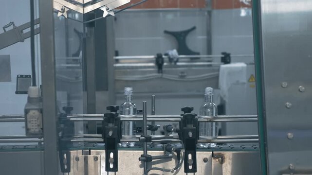 Automated bottling line moves transparent bottles filled with clear liquid on conveyor, industrial filling and packaging production inside beverage factory.