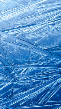 Ice frozen in intricate patterns of delicate crystals with brilliant contrasts of deep blues. Real unique patterned crystal formations. Sparkling window frost or icy cold winter frosting background.