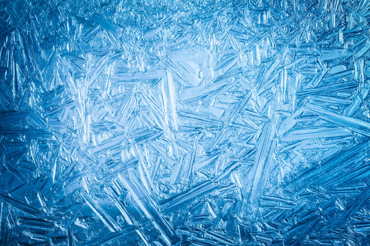 Ice frozen in intricate patterns of delicate crystals with brilliant contrasts of deep blues. Real unique patterned crystal formations. Sparkling window frost or icy cold winter frosting background.
