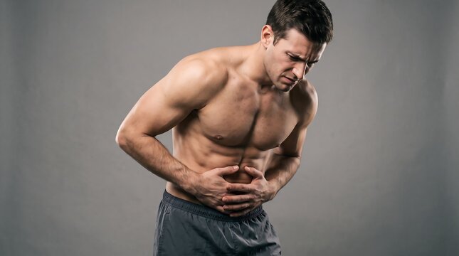 Suffering Healthcare and Medicine Concept of Athletic Shirtless Man Holding Stomach in Severe Abdominal Pain, Cramp, or Indigestion Against Grey Studio Background