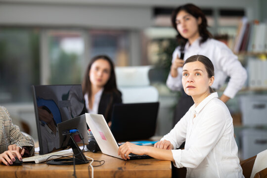Interested middle-aged woman watching visual demonstration with colleagues during project presentation in modern office