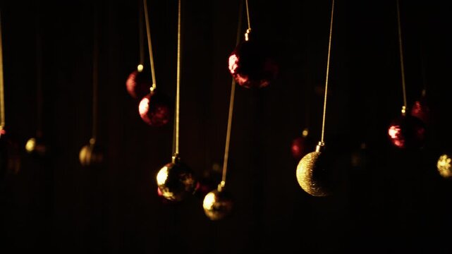 In front of a black background, Christmas balls swing slowly hanging from a wire