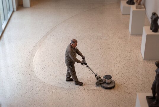 High angle view of a professional male cleaner polishing a terrazzo floor using an electric buffer machine in a modern museum gallery