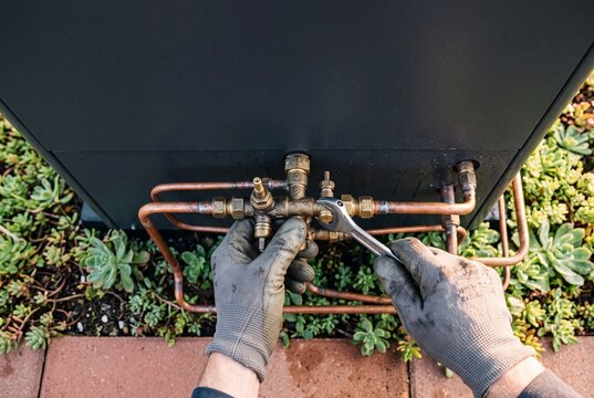 Close Up of Technician Hands in Work Gloves Using Wrench to Install or Repair Copper Pipes on Outdoor HVAC Heat Pump System