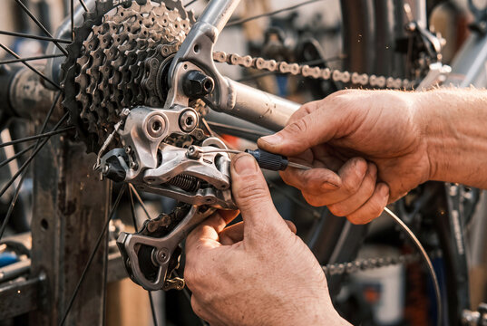 Bicycle mechanic hands adjusting the rear derailleur cable during gear tuning and bike maintenance in a workshop